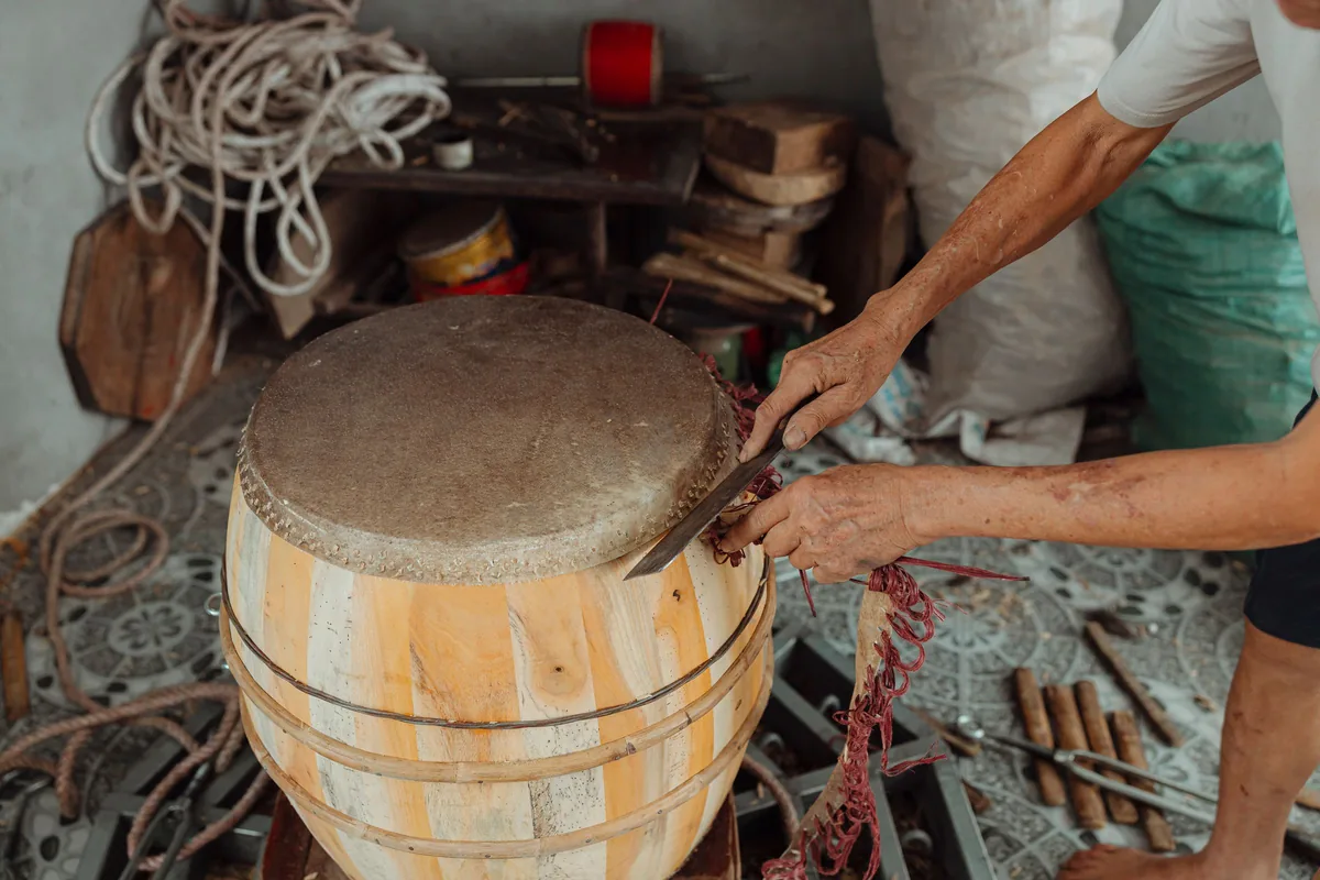 Manos trabajando sobre un tambor de duelas de madera clara con una membrana natural sujeta al borde